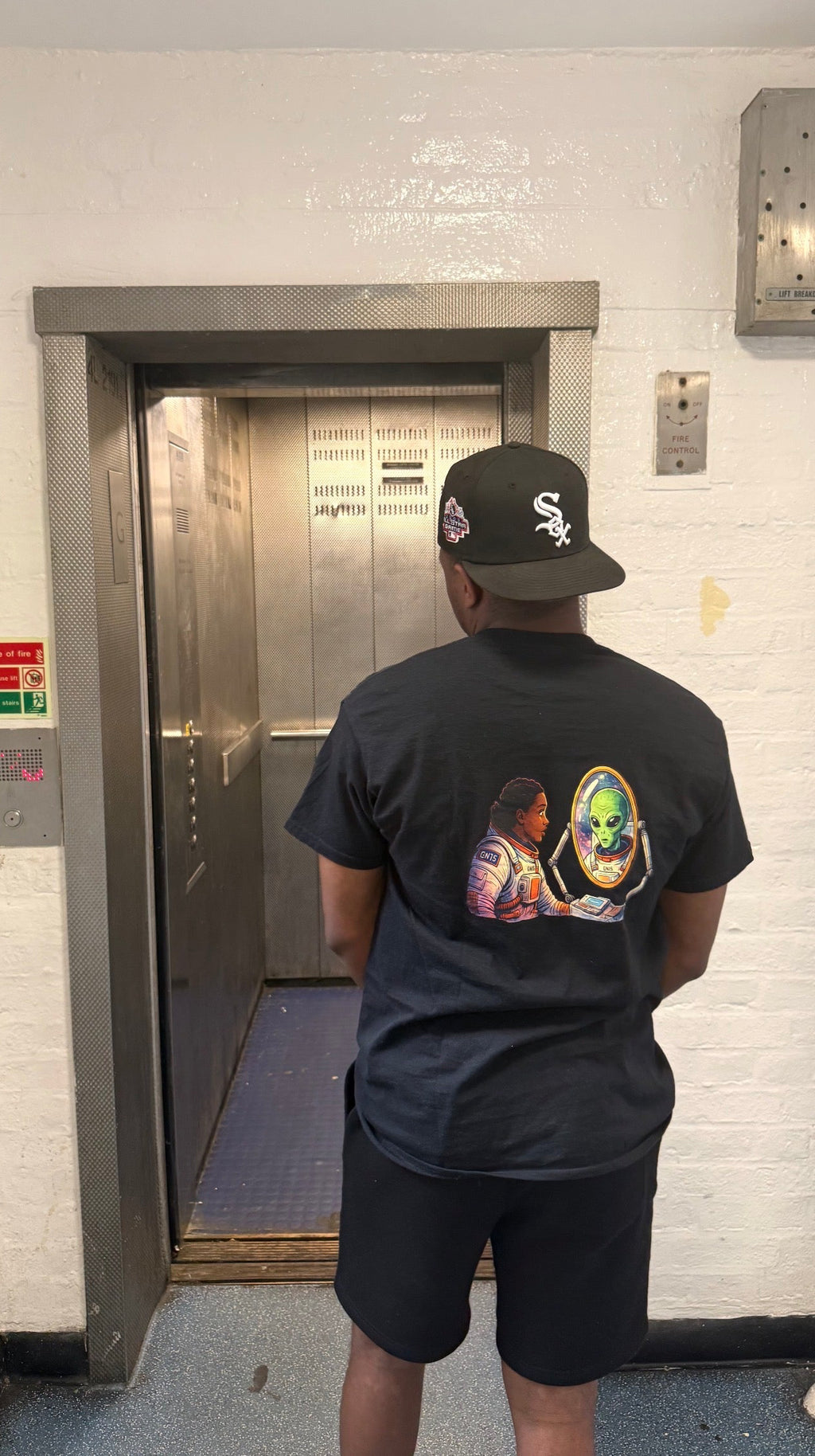 Model wearing the black GN15 Cosmic Reflection astronaut graphic tee with alien mirror artwork on the back